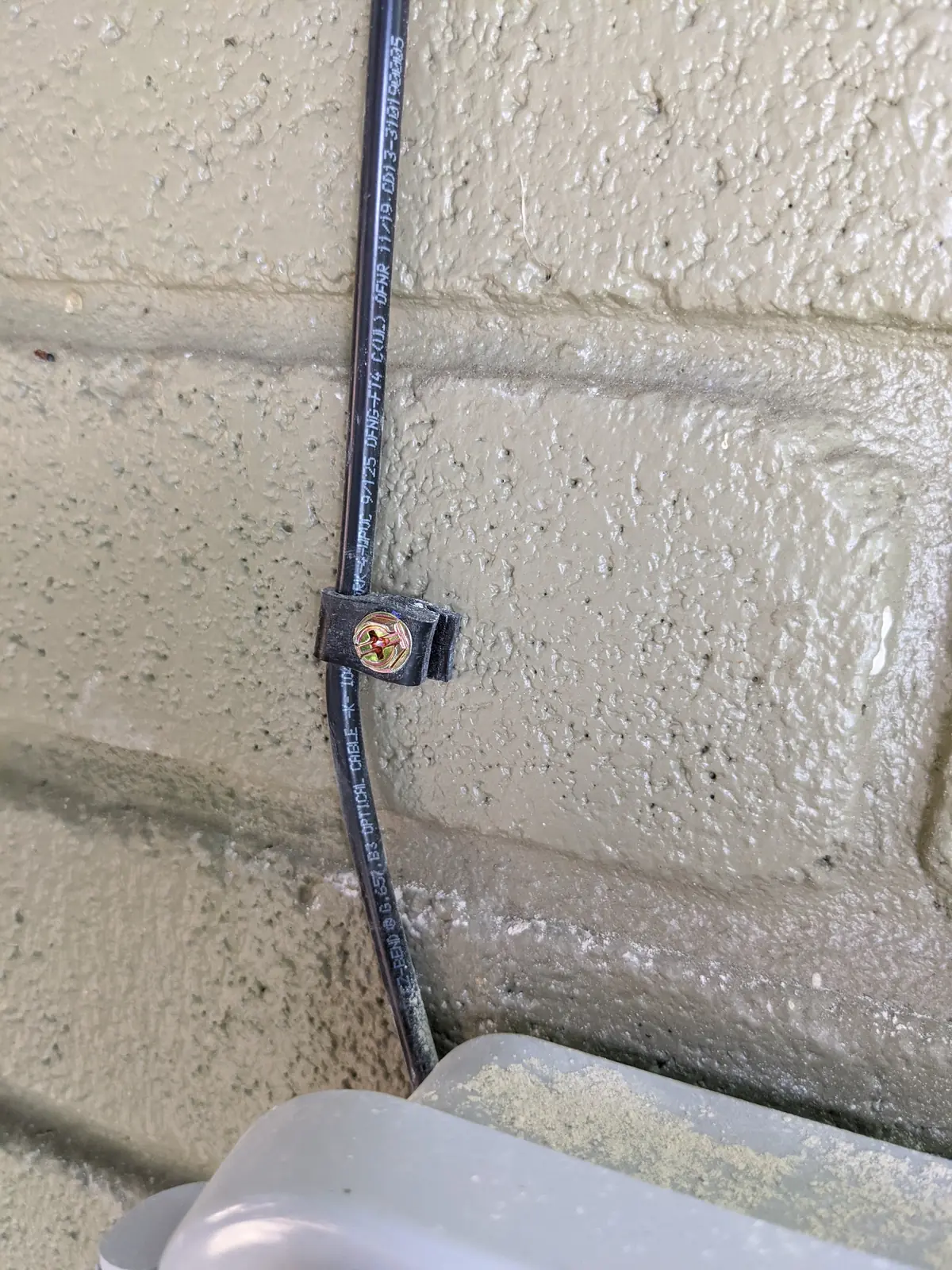 Single cable run fastened to a painted block wall with a mounting clamp
