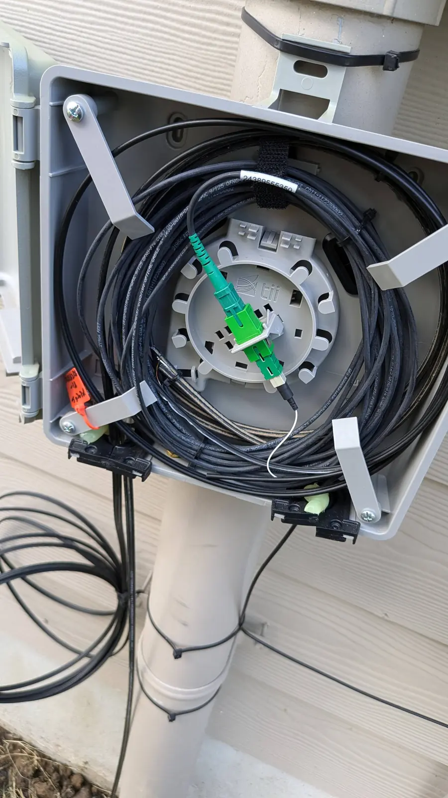 Wall-mounted fiber splice closure opened to show coiled fiber slack and green SC/APC connector